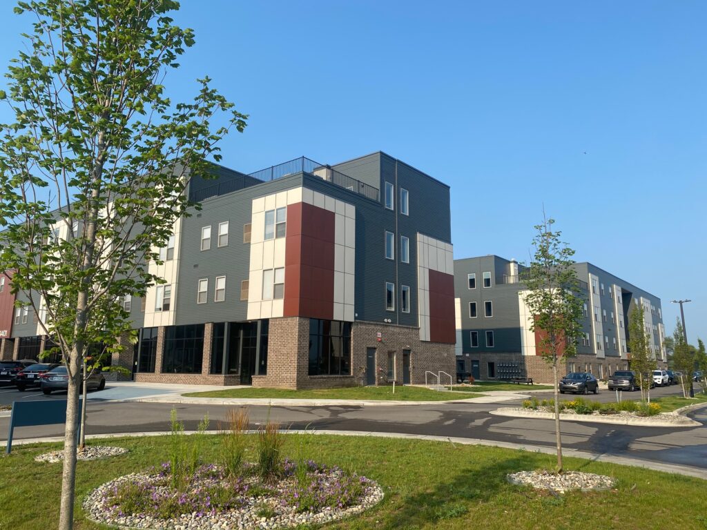 Affordable housing apartment building with a parking lot of cars outside.