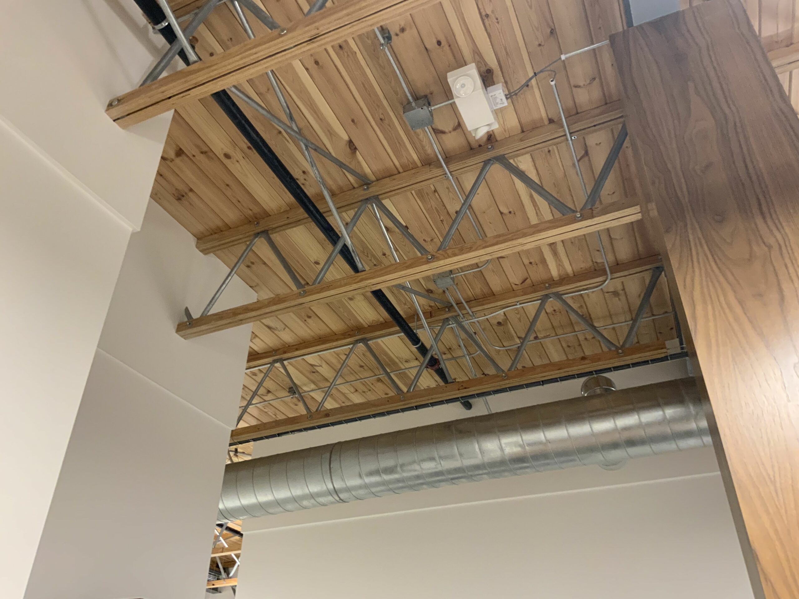 The ceiling of the Crahen Office Building. Clean wood panels, rafters, and exposed ductwork can be seen.