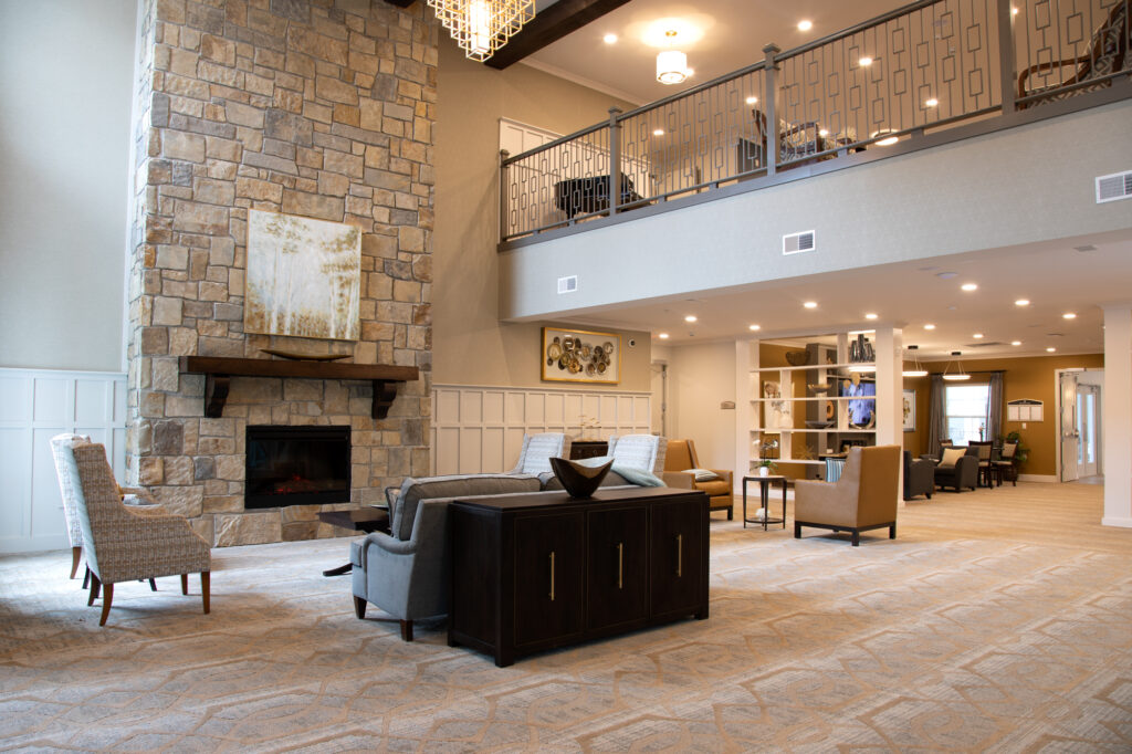 Brightly lit open sitting room around a fireplace. An upper story, bookcase, and additional sitting room can also be seen.