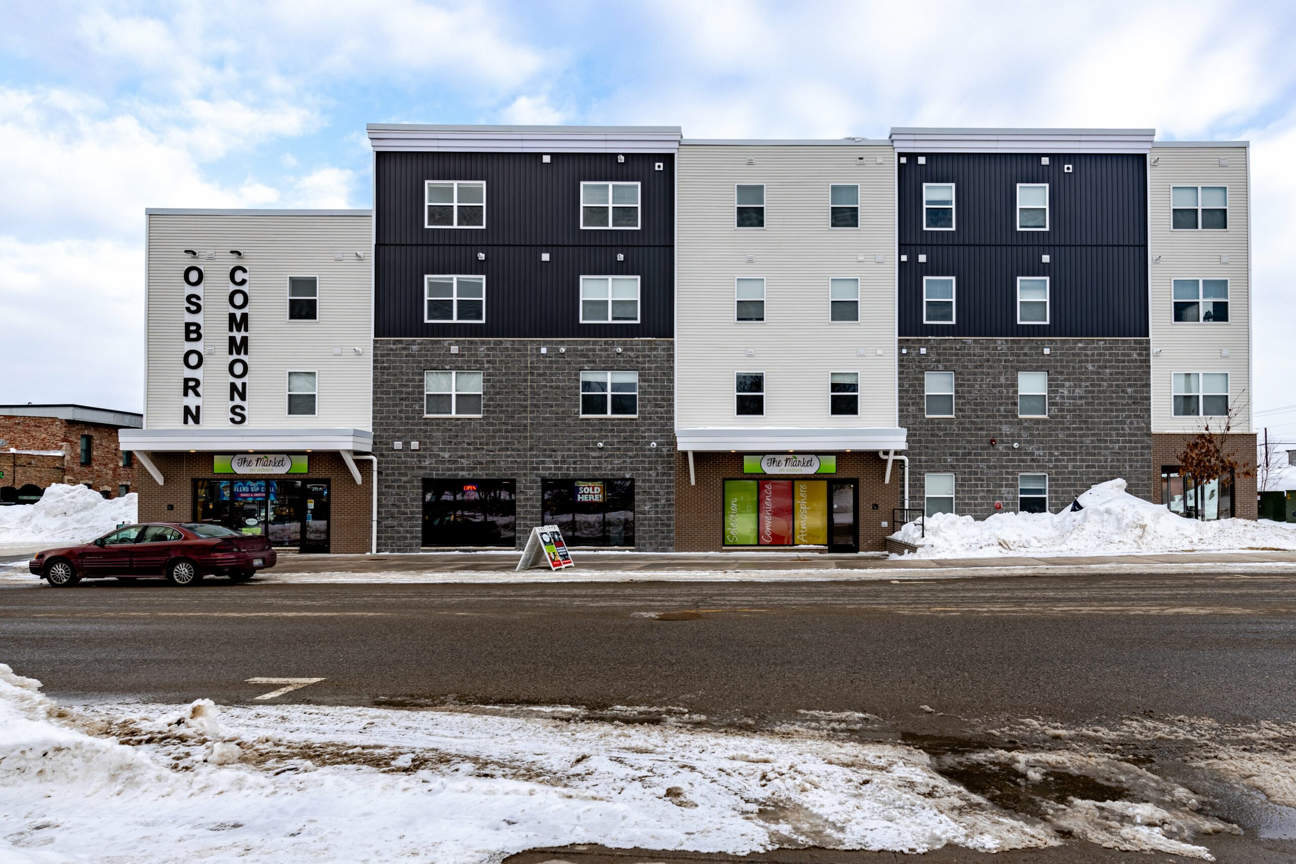 Ground level view of the apartment building, Osborn Commons and building's market storefront on a winter day