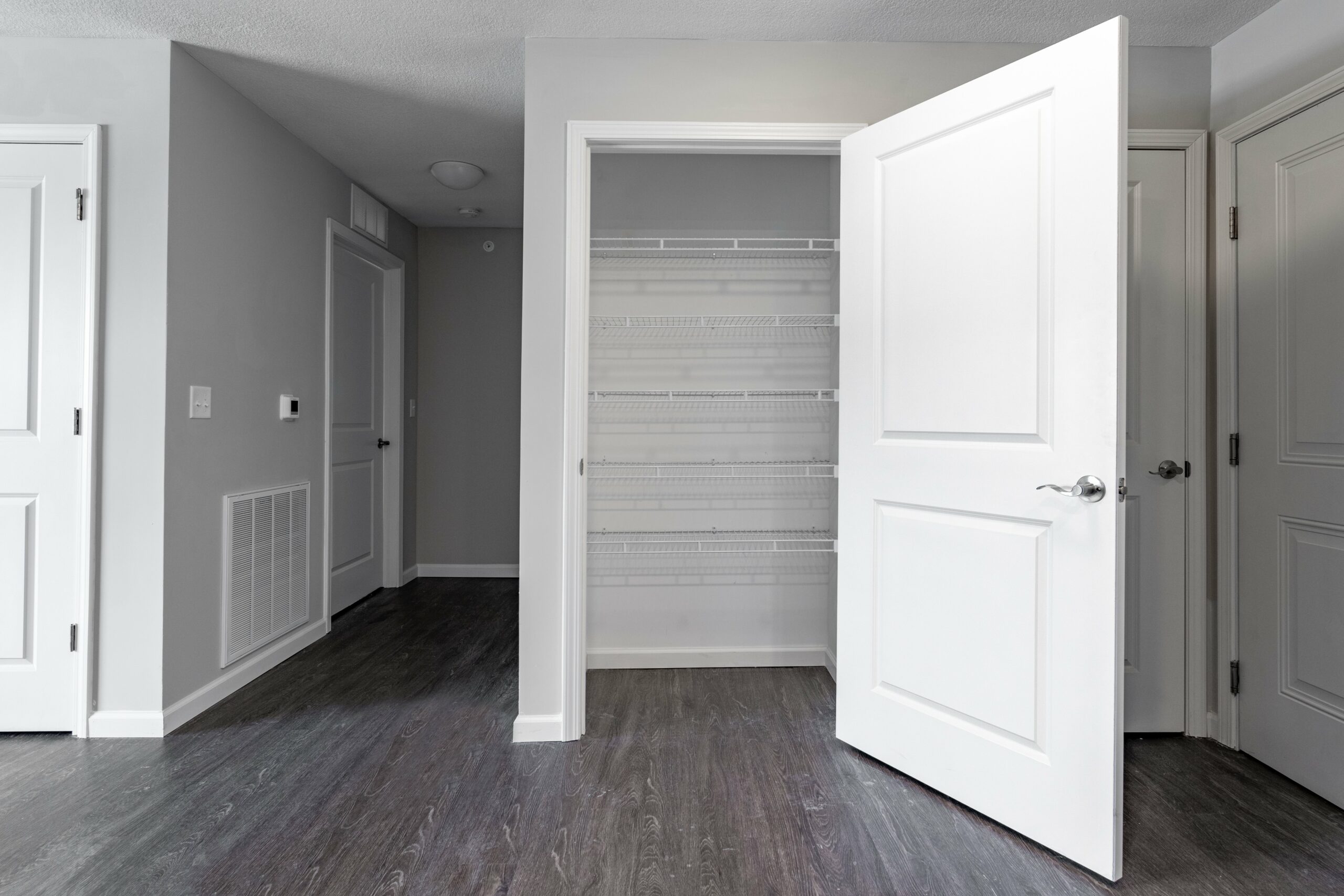 Open-concept main living space with linen closet, hallway, and two doors leading to bedrooms in an Osborn Commons apartment unit