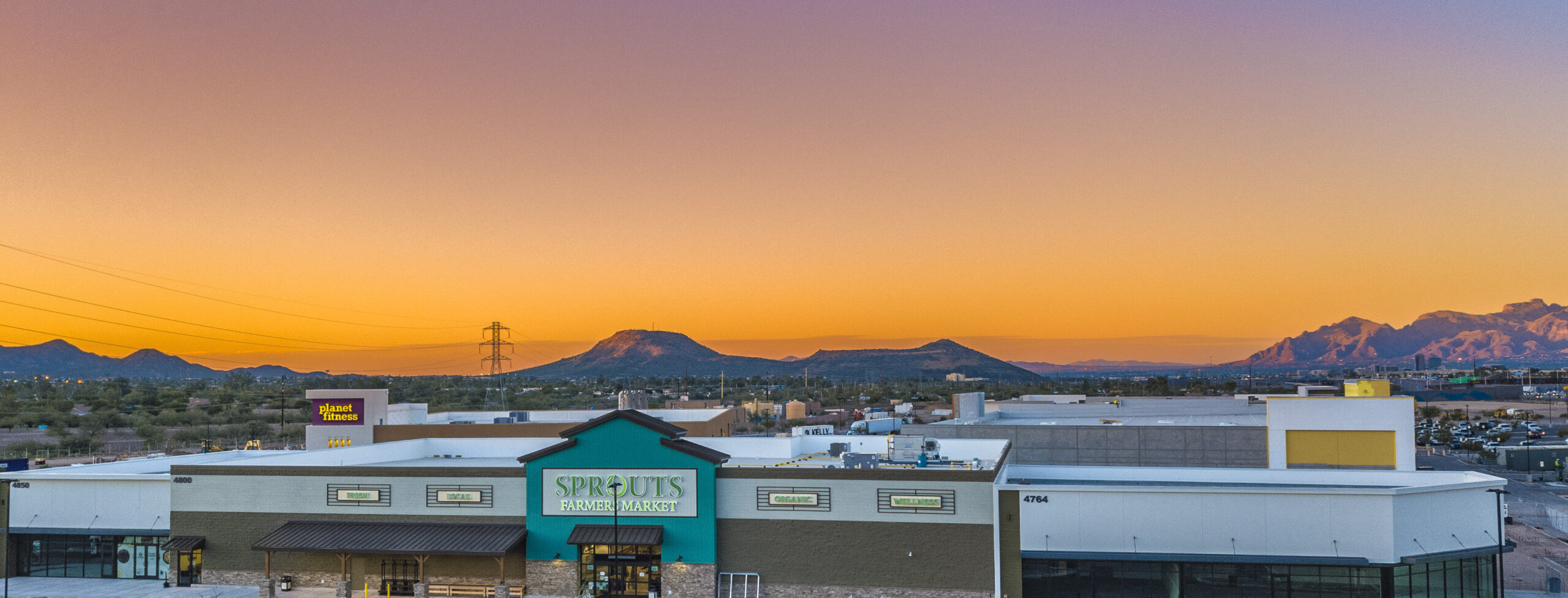 An aerial view of Sprouts Farmers Market, with mountains and the sunset in the background.