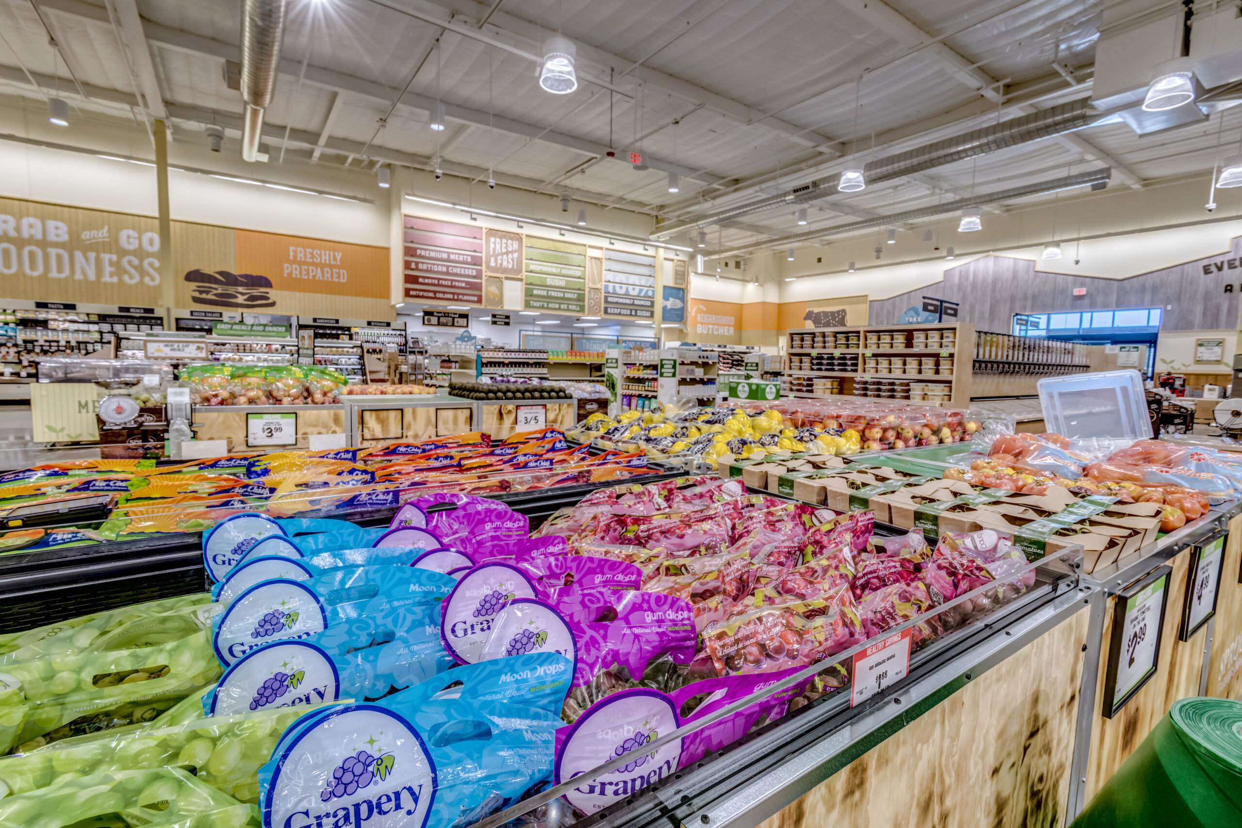 Produce aisle at Sprouts Farmers Market, displaying fresh grapes, tomatoes, and other produce.