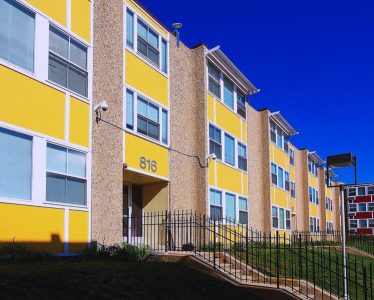 Exterior of a large multi-story yellow apartment building, extending out of the scene.
